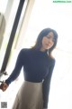 A woman standing in front of a window wearing a skirt.