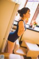 A woman in a black bathing suit standing in front of a refrigerator.