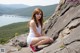 A young woman sitting on top of a large rock.