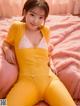 A woman in a yellow bodysuit sitting on a pink bed.