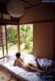 A naked woman laying on a bed in front of a window.