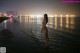 A naked woman standing in the water at night.