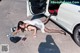 A woman laying on the ground next to a white car.