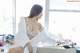 A woman in a white robe sitting on a window sill.