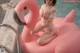 A woman in a white bathing suit sitting on an inflatable flamingo.